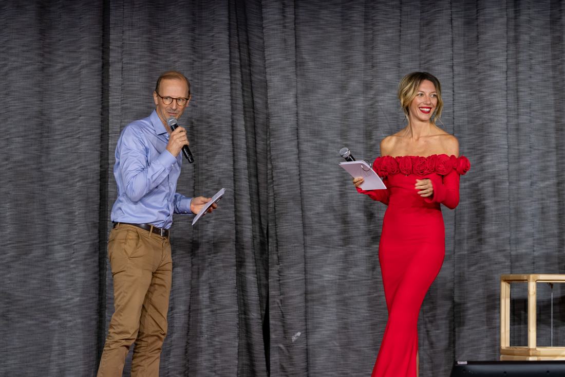 Salomé en robe rouge longue sur scène avec son co-présentateur